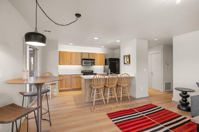 kitchen with black appliances, light brown cabinets, light wood-type flooring, and a breakfast bar area