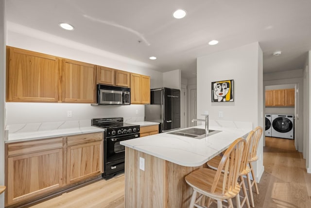 kitchen featuring black stove, sink, independent washer and dryer, light wood-type flooring, and kitchen peninsula