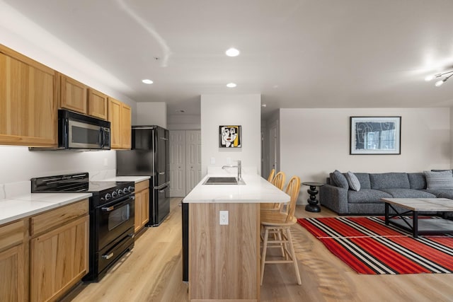 kitchen featuring black appliances, sink, light hardwood / wood-style flooring, a kitchen island, and a breakfast bar area