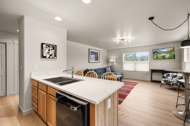 kitchen with a breakfast bar, sink, black dishwasher, and light hardwood / wood-style flooring