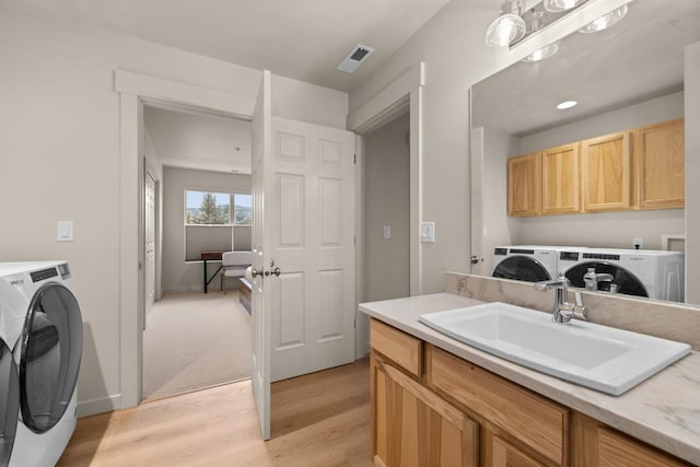 clothes washing area with washer and clothes dryer, cabinets, light wood-type flooring, and sink