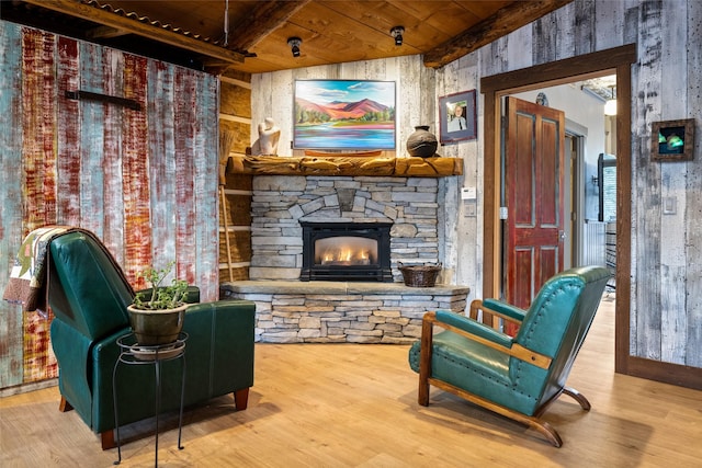 living area with hardwood / wood-style flooring, a stone fireplace, beam ceiling, and wooden ceiling