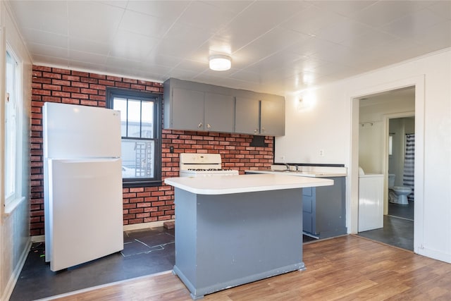 kitchen with gray cabinetry, brick wall, white refrigerator, hardwood / wood-style flooring, and range