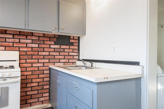 kitchen with gray cabinetry, sink, brick wall, and white range