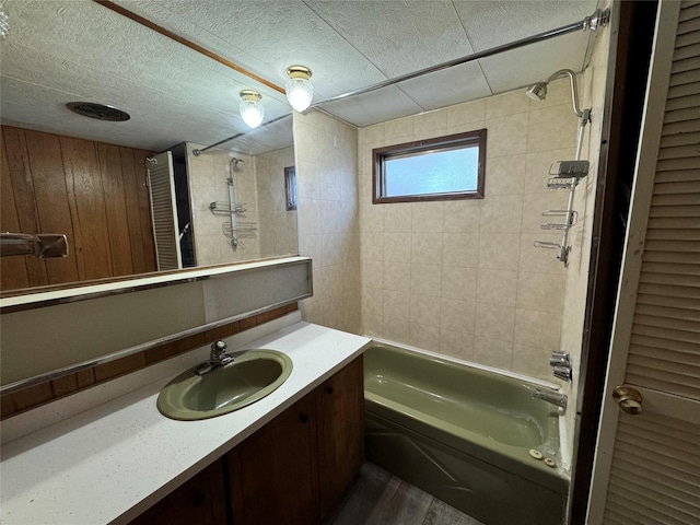 bathroom with wood walls, vanity, wood-type flooring, and tiled shower / bath