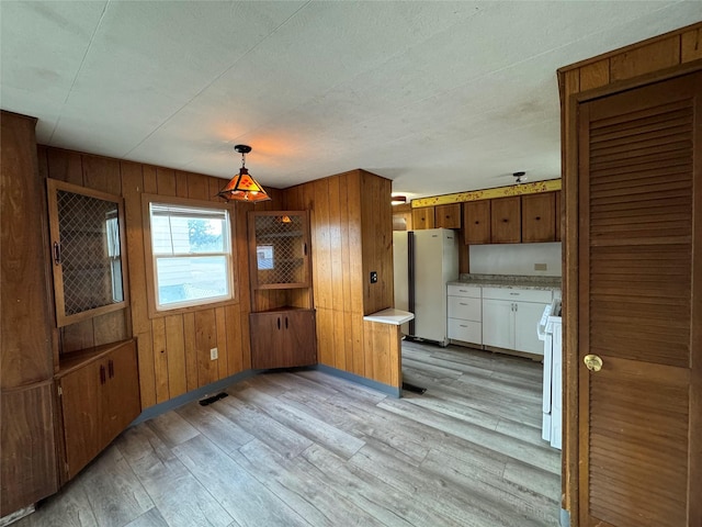 kitchen with wooden walls, light hardwood / wood-style flooring, pendant lighting, and white appliances