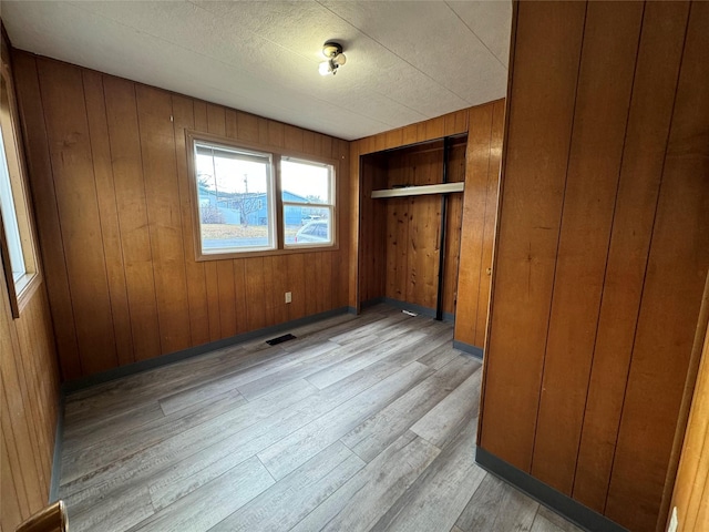 unfurnished bedroom featuring light hardwood / wood-style flooring, a closet, and wood walls