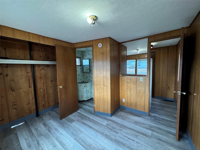 unfurnished bedroom featuring a textured ceiling, ensuite bathroom, hardwood / wood-style flooring, and wooden walls