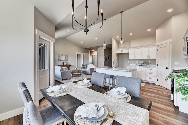 dining space with a notable chandelier, light hardwood / wood-style floors, sink, and vaulted ceiling