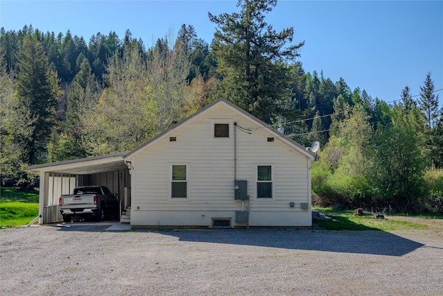 view of side of home with a carport, a forest view, and gravel driveway