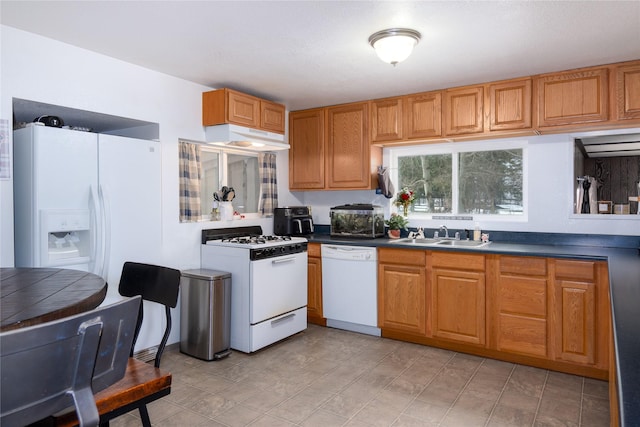 kitchen with under cabinet range hood, brown cabinetry, white appliances, a sink, and dark countertops