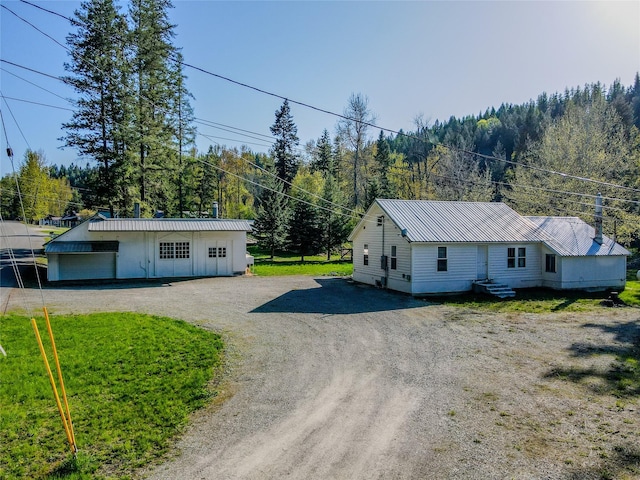 view of front of house with metal roof, a view of trees, and driveway