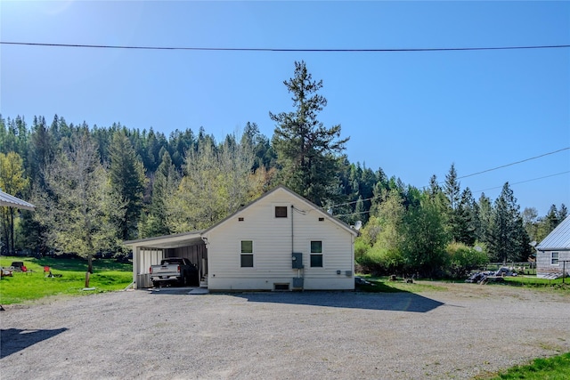 view of side of home with a forest view and gravel driveway