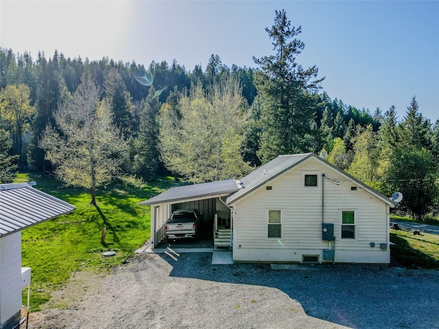 view of front of property with driveway, a view of trees, a front lawn, and a carport