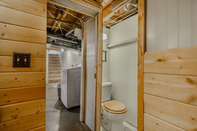 bathroom featuring washer / clothes dryer, wooden walls, concrete flooring, and toilet