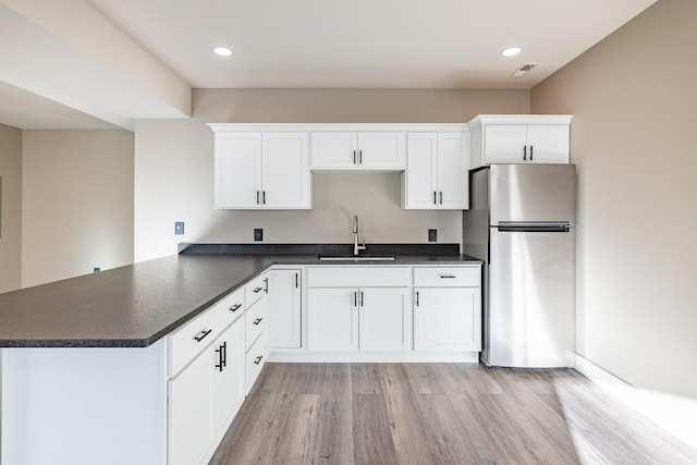 kitchen featuring white cabinets, kitchen peninsula, stainless steel refrigerator, and sink