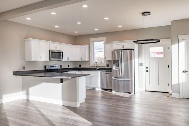 kitchen featuring kitchen peninsula, appliances with stainless steel finishes, light wood-type flooring, decorative light fixtures, and white cabinets