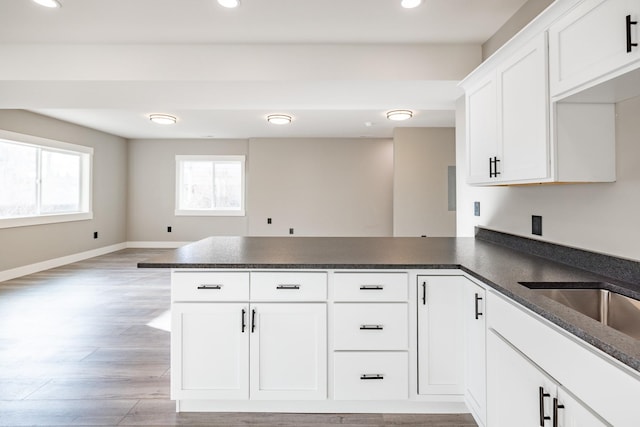 kitchen with kitchen peninsula, light hardwood / wood-style floors, white cabinetry, and sink