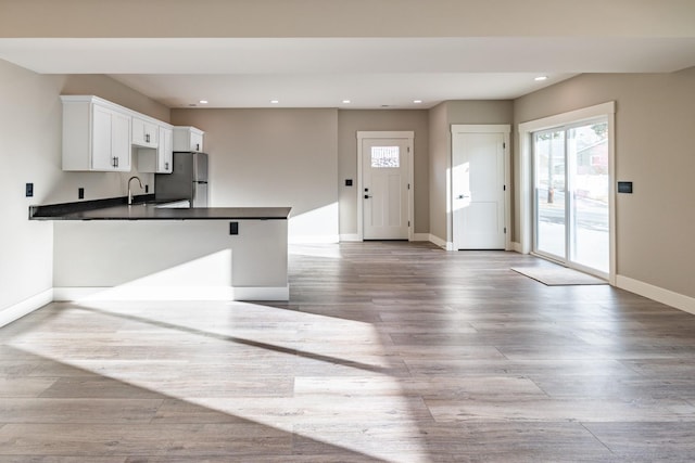 kitchen featuring sink, kitchen peninsula, stainless steel fridge, light hardwood / wood-style floors, and white cabinetry