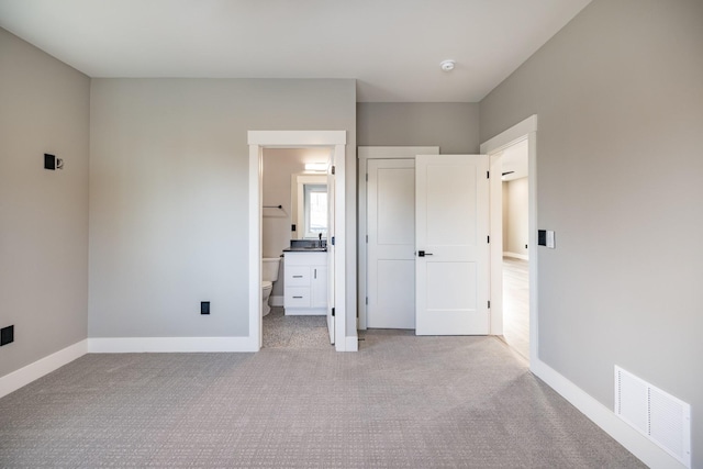 unfurnished bedroom featuring ensuite bathroom and light colored carpet