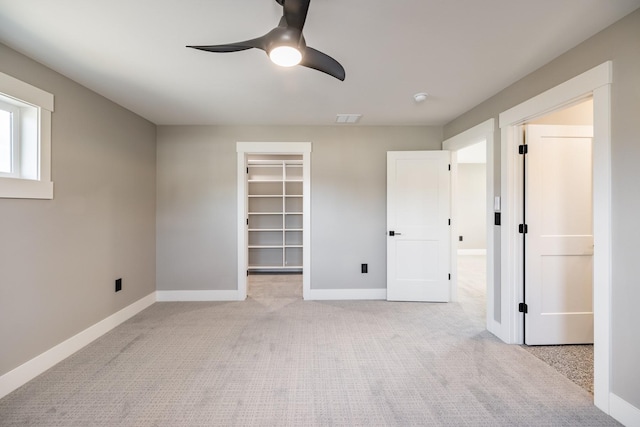 unfurnished bedroom with a spacious closet, a closet, ceiling fan, and light colored carpet