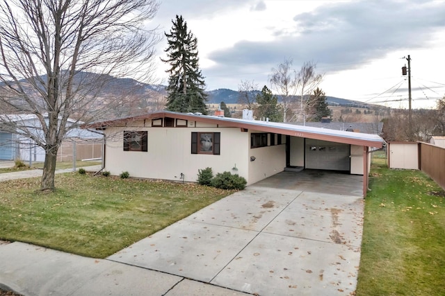 single story home featuring a mountain view, a front lawn, a storage unit, and a carport