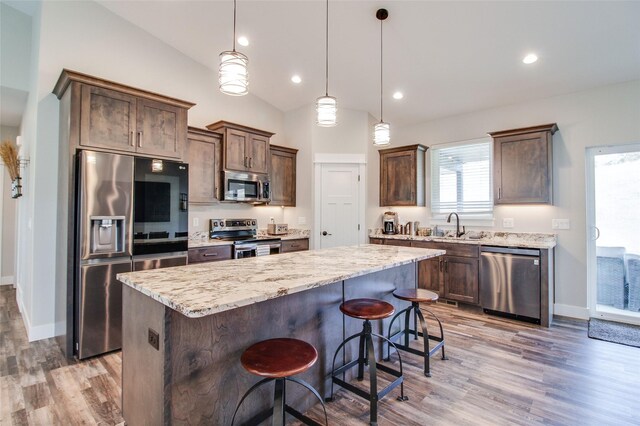 kitchen with a center island, hanging light fixtures, a breakfast bar, appliances with stainless steel finishes, and light wood-type flooring