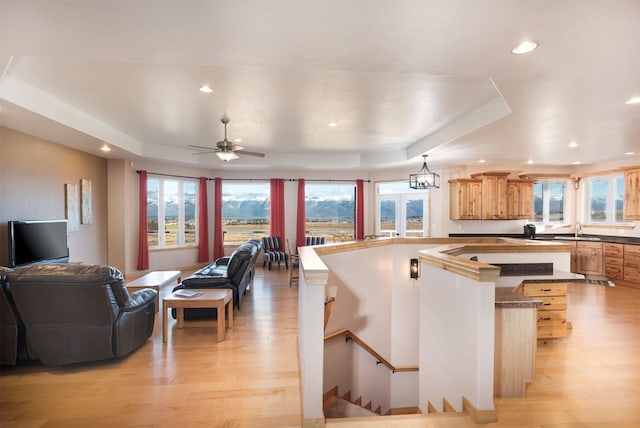 kitchen featuring ceiling fan with notable chandelier, light hardwood / wood-style floors, a raised ceiling, and sink