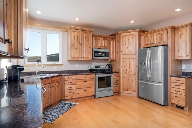 kitchen with dark stone countertops, sink, light hardwood / wood-style flooring, and appliances with stainless steel finishes