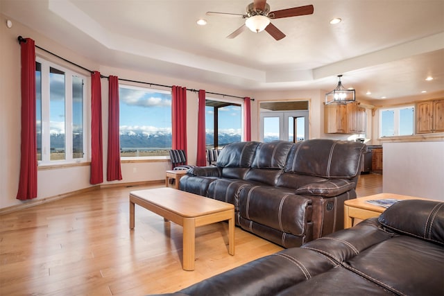 living room featuring ceiling fan with notable chandelier, light wood-type flooring, and a tray ceiling