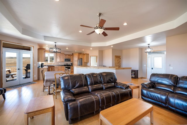 living room with french doors, a tray ceiling, ceiling fan, and light hardwood / wood-style floors