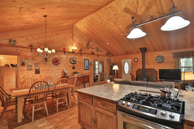 kitchen featuring decorative light fixtures, wood walls, hardwood / wood-style flooring, stainless steel gas range, and a wood stove