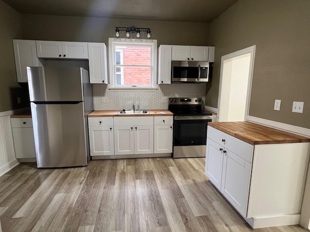 kitchen with wood counters, appliances with stainless steel finishes, tasteful backsplash, sink, and white cabinets