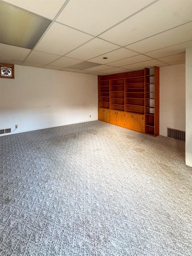 basement featuring a drop ceiling, carpet floors, and built in shelves