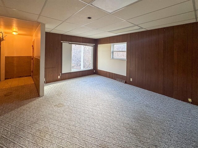 unfurnished room featuring carpet floors, a drop ceiling, and wood walls