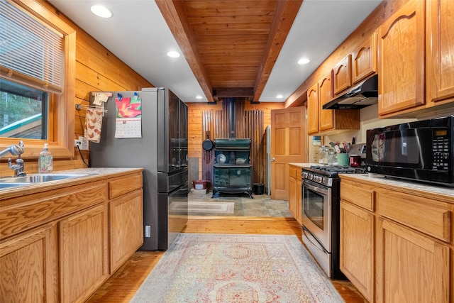 kitchen featuring a wood stove, appliances with stainless steel finishes, wooden walls, beamed ceiling, and light wood-type flooring