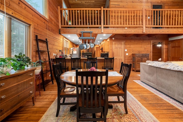 dining room with light wood-type flooring, a high ceiling, and wood walls