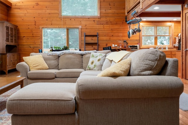 living room featuring a towering ceiling, plenty of natural light, light hardwood / wood-style floors, and wooden walls