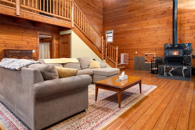 living room featuring hardwood / wood-style floors, wood walls, a high ceiling, and a wood stove