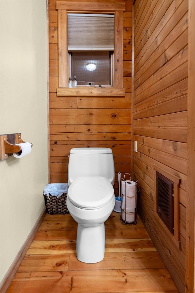 bathroom with wood-type flooring, toilet, and wood walls