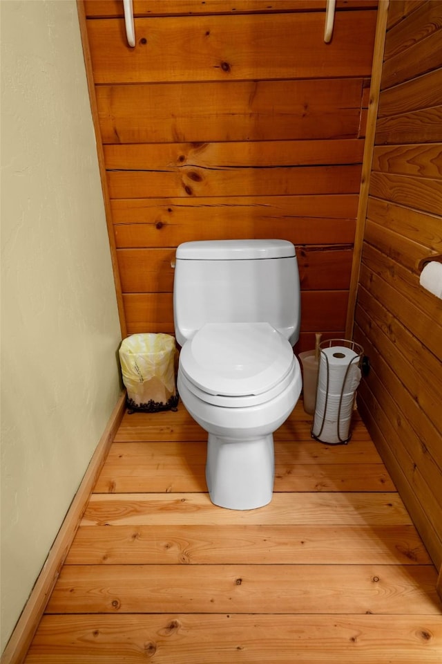 bathroom with wood-type flooring, wooden walls, and toilet