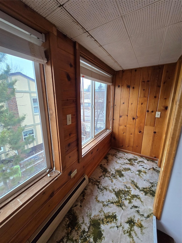 interior space with wooden walls, carpet floors, and a baseboard heating unit