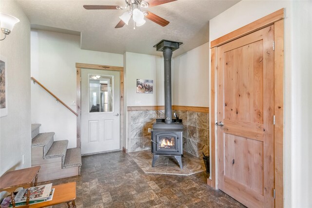 living room featuring a textured ceiling, a wood stove, ceiling fan, and tile walls