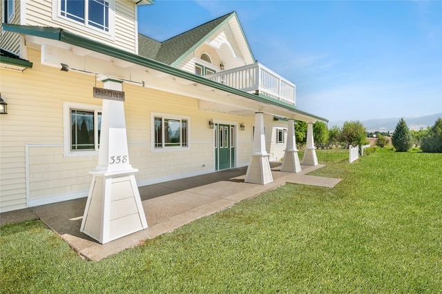 back of house featuring a lawn and a balcony