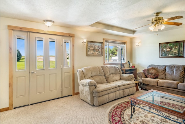 living room with a tray ceiling, ceiling fan, light colored carpet, and a textured ceiling