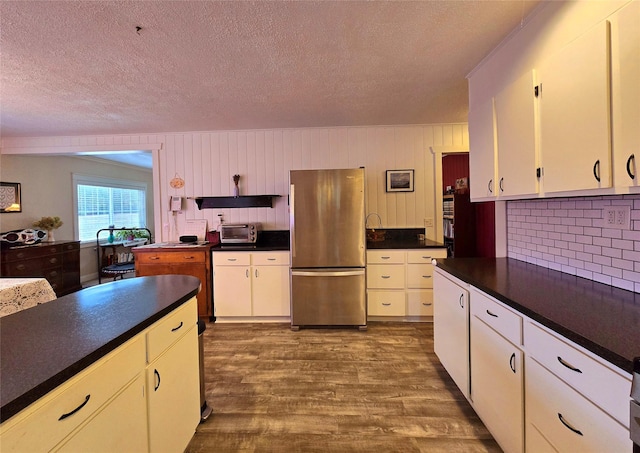 kitchen with hardwood / wood-style flooring, stainless steel fridge, white cabinetry, and a textured ceiling