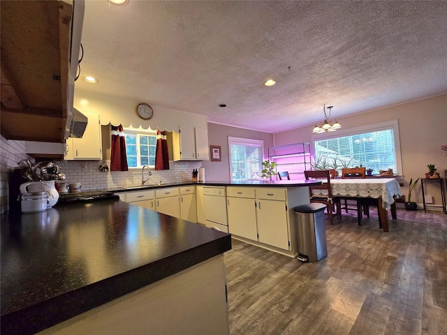 kitchen with tasteful backsplash, kitchen peninsula, dark wood-type flooring, and an inviting chandelier