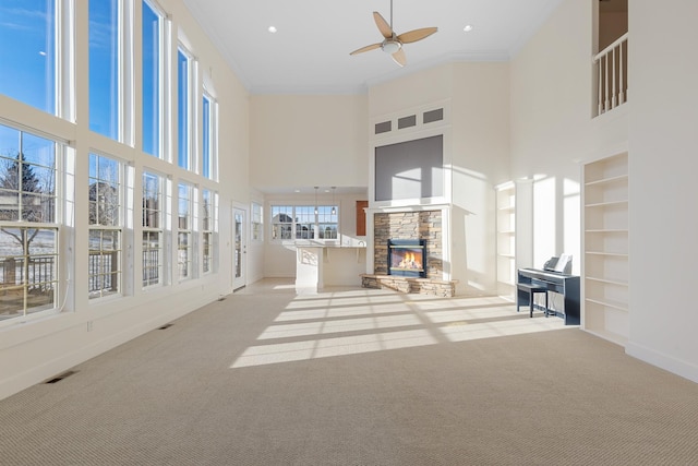 unfurnished living room with light carpet, built in shelves, ceiling fan, crown molding, and a fireplace