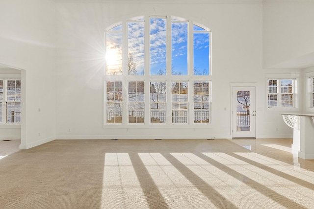 unfurnished living room featuring light colored carpet and a high ceiling