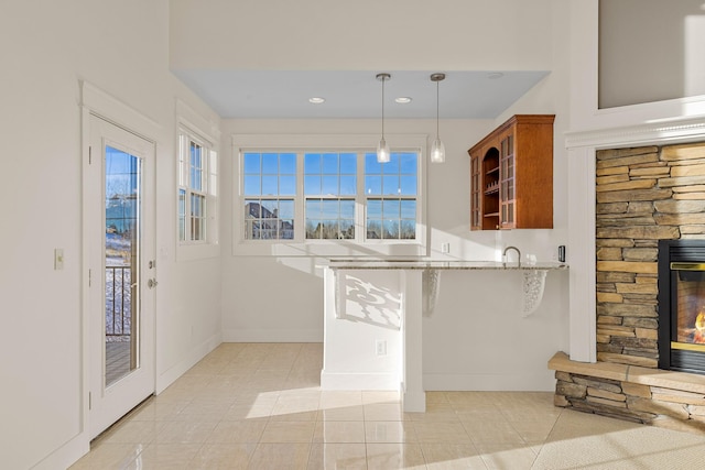 kitchen featuring a stone fireplace, light tile patterned floors, decorative light fixtures, kitchen peninsula, and a breakfast bar area